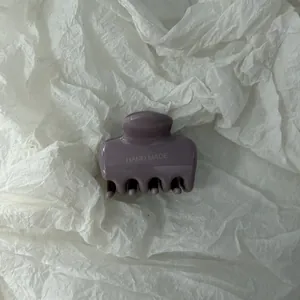 Primo piano di un fermaglio per capelli malva lucido con scritta "HAND MADE" su carta bianca