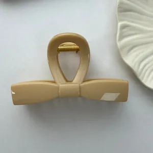 Detail view of a large creamy beige bow-shaped hair claw clip with a glossy finish.