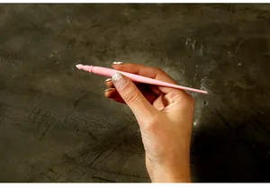 Detail view showing a hand holding a pink plastic stylus scratch pen for art paper