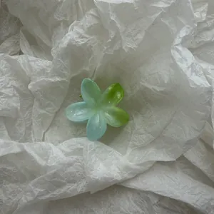 Detail van een plumeria bloem haarklem met blauw en groen verloop op wit papier achtergrond