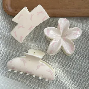Close-up of three cream-colored hair claw clips with pink bow patterns on a tray