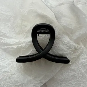 Close-up view of a minimalist matte black hair claw clip on white textured paper