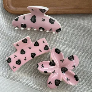 Detailed view of pink macaron hair claws featuring black heart and bow patterns