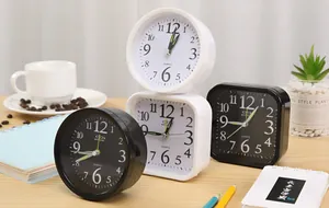 Close-up of minimalist black and white analog alarm clocks arranged on a wooden desk with props