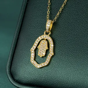 Detail of a gold Hamsa hand pendant necklace with sparkly pavé-set stones on a green box.