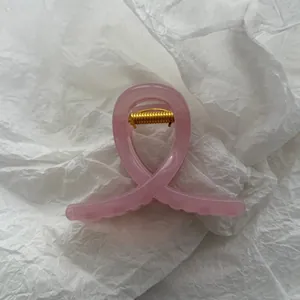 Close-up of a jelly pink cross-shaped hair claw clip on white wrinkled paper background.