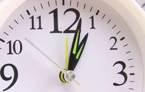 Close-up macro view of a minimalist white analog alarm clock face with colorful hands.
