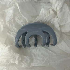 Primo piano dettagliato di una molletta per capelli grigia minimalista con scritta 'HAND MADE'