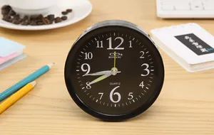Close-up of a stylish black minimalist alarm clock placed on a wooden desk with props