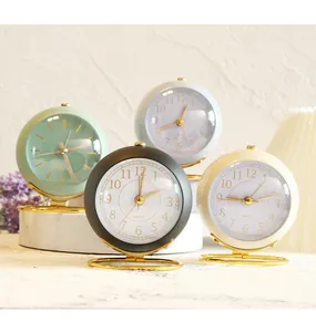 Detail view of four minimalist mini desk alarm clocks in assorted colors with gold stands