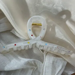 Close-up detail of white acetate shark hair clip with sparkling multi-colored rhinestones