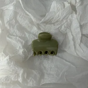 Dettaglio macro di un fermaglio per capelli verde oliva su uno sfondo bianco strutturato e ruvido