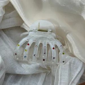 Detail of translucent white hair claw clip with multi-color rhinestones on fabric background