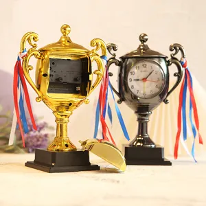 Decorative trophy-shaped bedside alarm clocks in gold and metallic finishes with ribbons