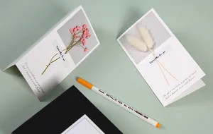Detail shot of elegant white greeting cards featuring real dried flowers and English quotes.