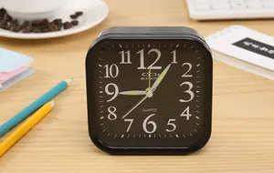 Detailed view of a minimalist black square quartz desk alarm clock on a wooden tabletop.