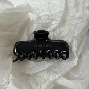 Detailopname van een gladde zwarte haarklem met HAND MADE gravering op wit papier