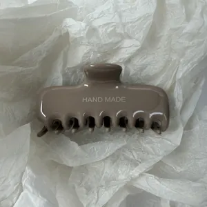 Close-up van een grote glanzende taupe haarklem met HAND MADE tekst op een getextureerde achtergrond
