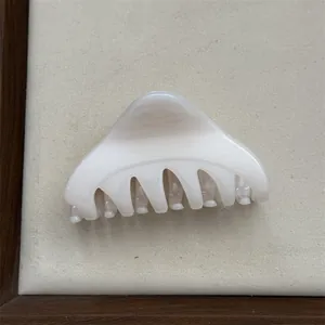 Detail view of a minimalist cream triangular hair claw clip on a soft beige display mat.