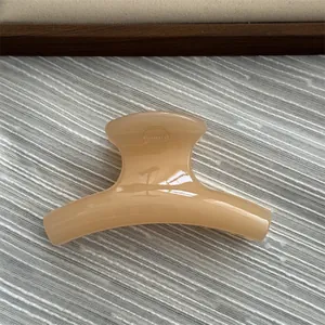 Close-up view of a small beige jelly-textured curved hair claw clip on textured grey fabric