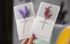 Detailed close-up of elegant greeting cards with real dried purple and red flowers.