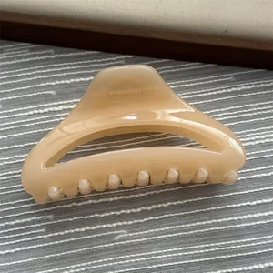 Close-up of a minimalist beige resin shark hair claw clip on textured background