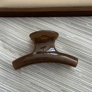 Close-up of a small glossy brown acrylic hair claw clip on a textured fabric background