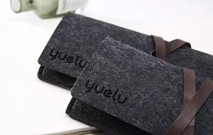 Dettaglio dell'astuccio in feltro nero con cinturino in pelle marrone e logo