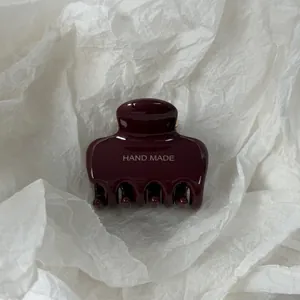 Detailopname van een glanzende bordeauxrode haarklem met zilveren HAND MADE belettering