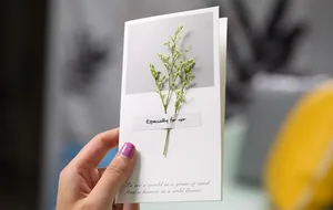Detail showing a real dried flower attached to a minimalist white greeting card.