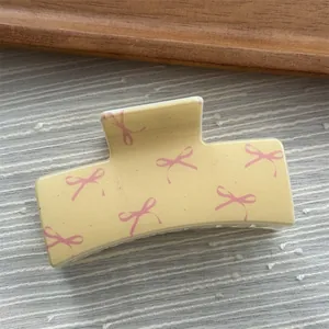 Macro view of a matte yellow hair claw clip decorated with delicate pink ribbon patterns
