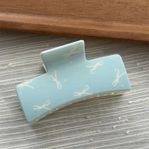 Macro view of light blue square hair claw clip with white ribbon bow print