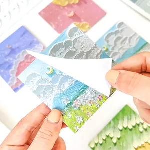 Hand peeling a cute oil painting style sticky note with cloud and flower landscape designs.