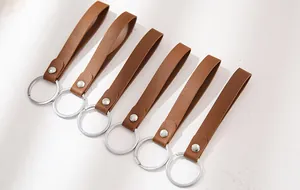 Detail view of six brown leather loop keychains with silver rings on light surface