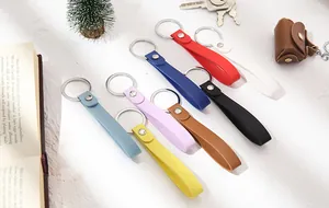Colorful handmade leather strap keychains displayed with lifestyle props on white desk.