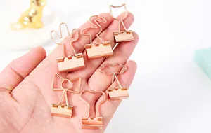 Kreative roségoldene Metall-Bindeklammern in verschiedenen Formen in der Hand