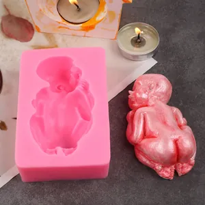 Detailed pink silicone baby-shaped mold displayed with a finished wax cast on a dark surface