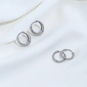 Primer plano de pendientes de aro de acero inoxidable plateado con diseño liso y trenzado