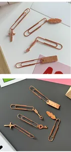 Vista detallada de clips metálicos de oro rosa con colgantes decorativos como cruz y pluma.