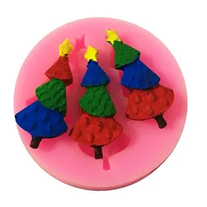 Primer plano de molde de silicona rosa con tres figuras de árbol de Navidad en fondant.