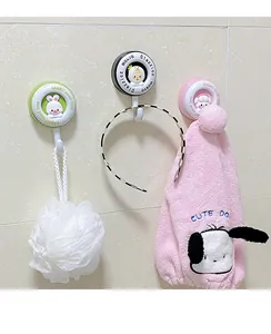 Close-up of cartoon adhesive hooks holding a bath sponge and a headband on a tiled wall