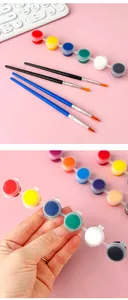 Mano che tiene un mini set di 6 colori acrilici con quattro pennelli per fai da te.