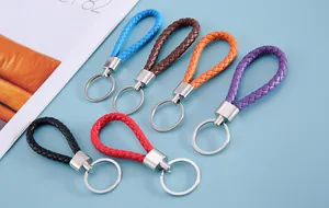 Six braided leather keychains in vibrant colors arranged on a light blue surface