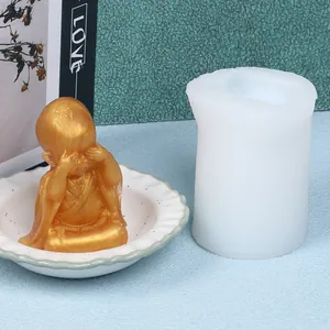 Close-up of a white silicone mold next to a finished gold-colored little monk figurine.