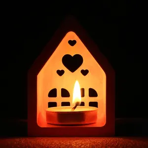 Detalle de un portavelas DIY en forma de casa con corazones y una vela encendida