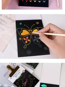 Close-up of a hand drawing a colorful butterfly on premium black scratch art paper