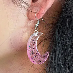 Dettaglio macro di un orecchino a mezzaluna rosa glitterato realizzato a mano in resina