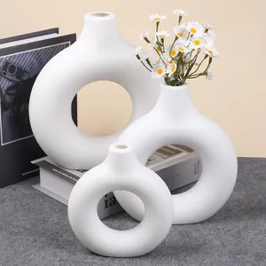 Set of three white donut-shaped decorative vases with daisies on a modern book stack