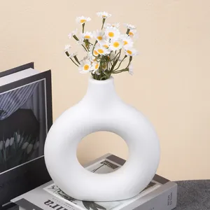 Minimalist white donut-shaped vase with flowers on a stack of books for home decor.