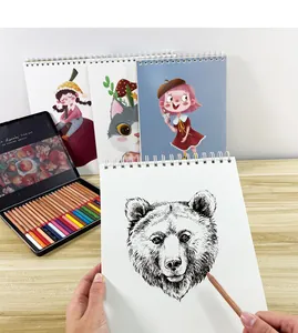 Detail shot of a hand sketching a bear on a spiral-bound A4 art sketchbook with pencils.